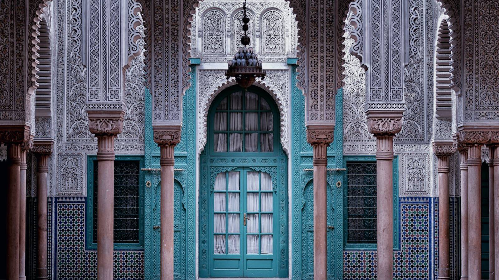 Portale ad arco con stucchi intagliati e zellige tradizionali marocchini, tra le colonne di un cortile storico